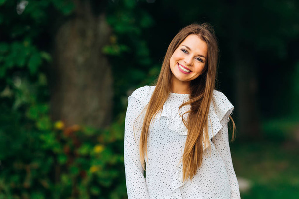 γνήσιο χαμόγελο του κοριτσιού που ντυμένοι στα λευκά ρούχα και κοιτάζει το φακό της κάμερας - Φωτογραφία, εικόνα