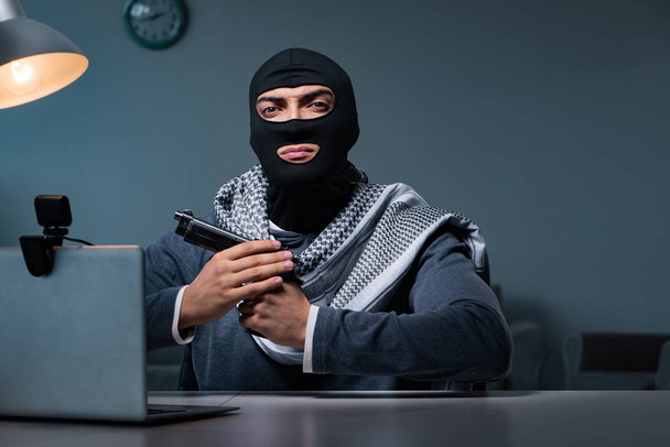 Terrorist burglar with gun working at computer - Photo, Image