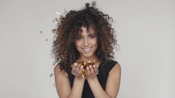 girl blowing confetti and smiling. portrait of a charming hispanic curly girl flying sequins and confetti. concept of the holiday, fun, celebrate. slow motion - Filmati, video