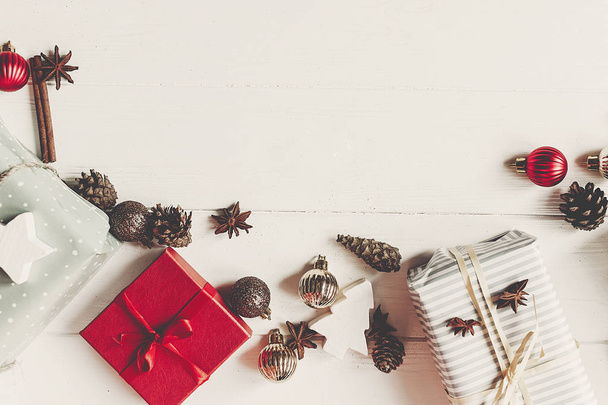 τυλιγμένο παρόντες κουτιά με στολίδια με κώνους γλυκάνισο σε άσπρο ξύλινες παρασκήνιο κάτοψη, χώρο για το κείμενο. Χριστούγεννα επίπεδη θέσει. Εποχιακοί Χαιρετισμοί κάρτα. Καλές Γιορτές - Φωτογραφία, εικόνα