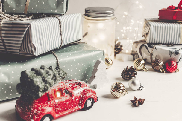 Feliz Navidad y feliz año nuevo. regalos modernos, adornos, juguete de coche con árbol, conos de anís y luces sobre fondo de madera blanca rústica. saludos de temporada. felices fiestas, tarjeta de Navidad
 - Foto, imagen