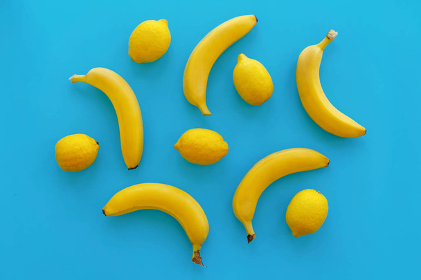 yellow bananas and lemons on bright blue paper, trendy flat lay. fruits modern image, top view. juicy summer vitamin abstract background. pop art style. minimalism pattern - Photo, Image