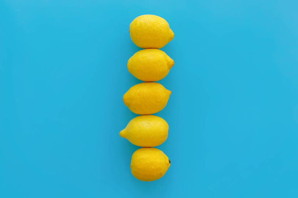 yellow  lemons in line  on bright blue paper, trendy flat lay. fruits modern image, top view. juicy summer vitamin and diet concept. pop art style. creative minimalism. space for text - Photo, Image