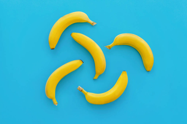 gele bananen op heldere blauwe papier, trendy achtergrond. vruchten modern plat lag. sappige zomer vitamine abstracte achtergrond, bovenaanzicht. pop-art stijl. banaan patroon. Blog - Foto, afbeelding