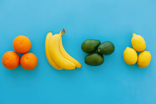 banane, arance, avocado e limoni gruppi su carta blu brillante, posa piatta alla moda. moderno concetto di immagine estiva. multi frutta piatto lay, succosa vitamina sfondo astratto
, - Foto, immagini