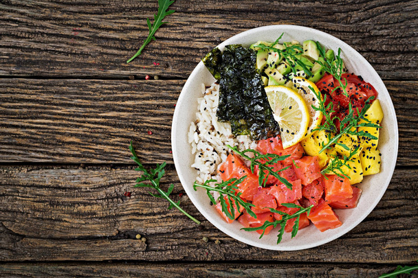 ご飯、アボカド、マンゴー、トマト、ゴマ、海藻とハワイアンのサーモン ピンクの魚突くボウル。鉢の石仏。ダイエット食品。平面図です。フラットを置く - 写真・画像