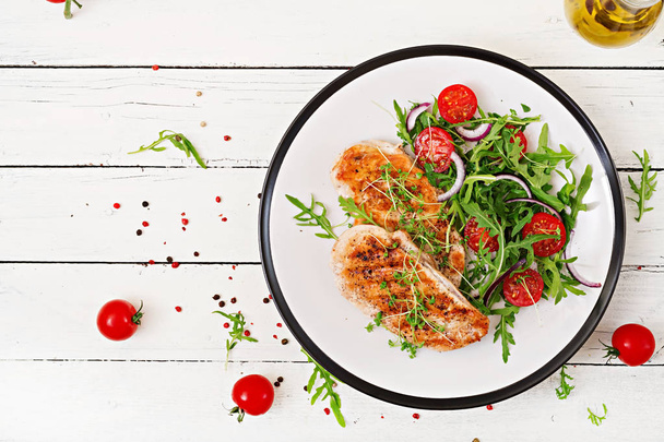 Gegrilde kip filets en vers fruit salade van tomaten, rode ui en rucola. Salade van kip vlees. Gezonde voeding. - Foto, afbeelding