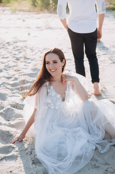 aantrekkelijke vrouw zittend op strand, vriendje lopen achter - Foto, afbeelding