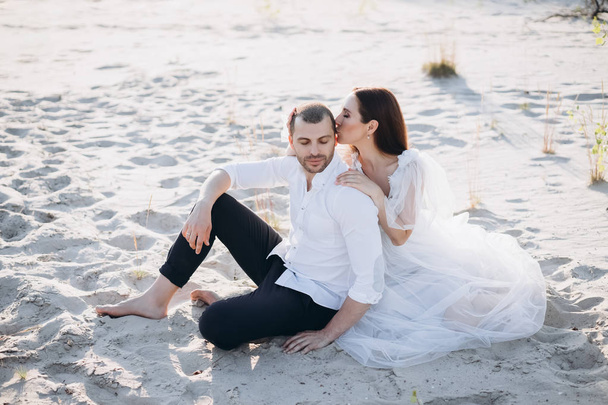 beautiful woman kissing her boyfriend while sitting on beach - Фото, зображення