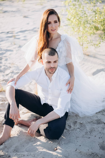 beautiful couple hugging and sitting on sand together - Photo, image