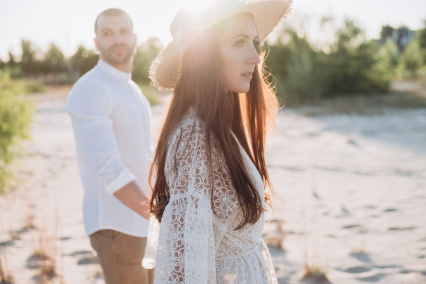 beautiful woman in hat holding hands with man on beach - Φωτογραφία, εικόνα