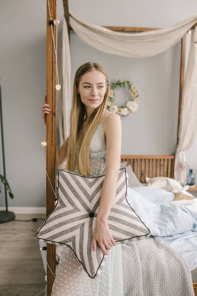hermosa joven mujer usando pijamas en la cama en casa está sosteniendo una almohada
 - Foto, imagen