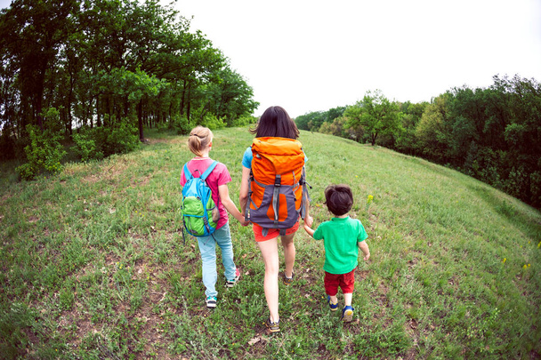 Kobiety z dziećmi idzie piesze wycieczki. Podróżowanie z rodziną. Chłopiec wychodzi z bratem i matką w lesie. Wycieczka z plecaki. - Zdjęcie, obraz