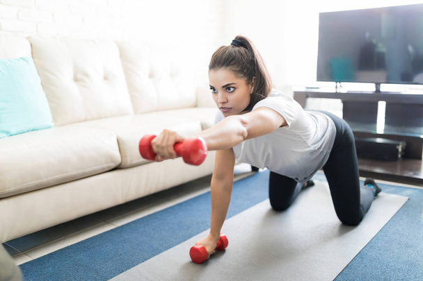 young hispanic woman training with dumbbells at home - Foto, imagen