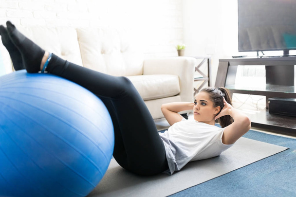 Подходящая женщина делает сидячие упражнения с мячом дома в гостиной
 - Фото, изображение