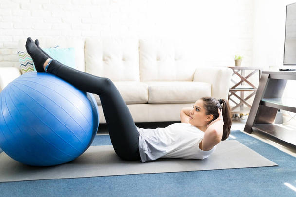 Fit latin woman doing sit ups with exercise ball at home in living room - Photo, Image