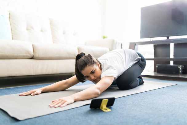 young latin woman watching online workout tutorials on smartphone at home - Foto, Imagem