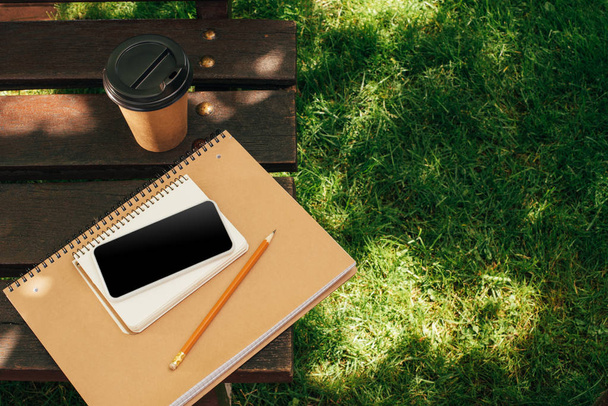 Nahaufnahme des Smartphones mit leerem Bildschirm, Notebooks und Coffee to go auf Holzbank - Foto, Bild