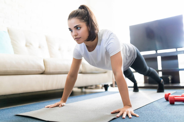 Giovane donna ispanica sana e forte che fa flessioni sul tappeto fitness in soggiorno
 - Foto, immagini
