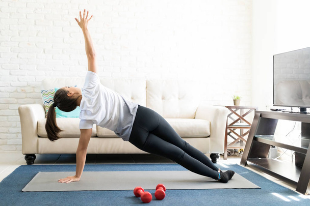 Задний вид женщины, делающей боковую доску йоги позы на коврик упражнения в гостиной
 - Фото, изображение
