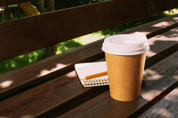 close up view of notebook with pencil and disposable cup of coffee on wooden bench - Foto, afbeelding