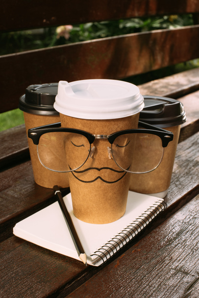 close up view of coffee to go, eyeglasses and notebook on wooden bench - 写真・画像