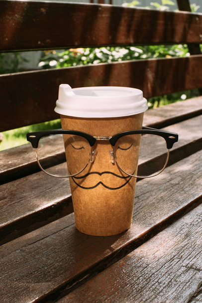 close up view of disposable cup with mustache sign and eyeglasses on wooden bench - 写真・画像