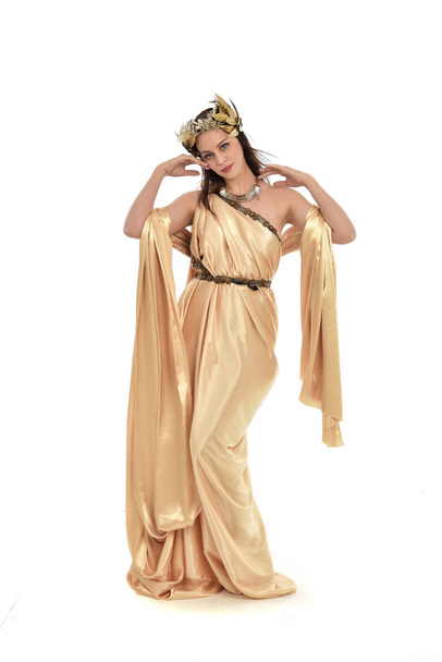 volledige lengte portret van brunette vrouw dragen gouden grecian jurk, staande pose. geïsoleerd op witte studio achtergrond. - Foto, afbeelding