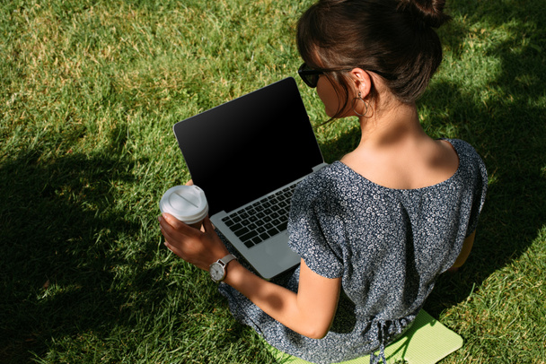 Achteraanzicht van freelancer met koffie te gaan werken op de laptop op groen gazon in een park - Foto, afbeelding