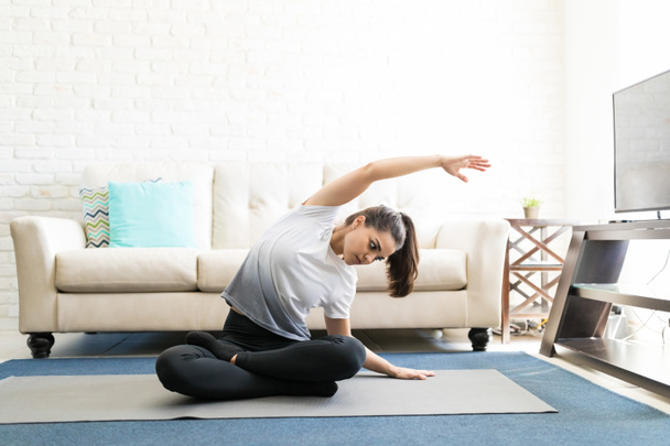 mujer joven y flexible sentada en una esterilla de yoga y doblada hacia los lados con los brazos extendidos
 - Foto, imagen