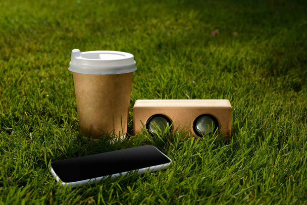 zblízka pohled na kávu s sebou, smartphone a audio reproduktor na zelené trávě - Fotografie, Obrázek