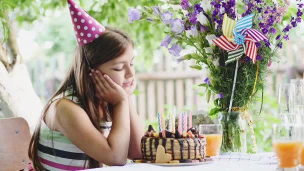 Boldog lány a kerti asztalnál ül és csodálja egy ünnepi torta - Felvétel, videó