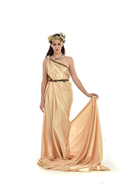 ブルネットの女性金のギリシャ ドレスを着てポーズを立っているの完全な長さの肖像画。ホワイト スタジオの背景に分離. - 写真・画像