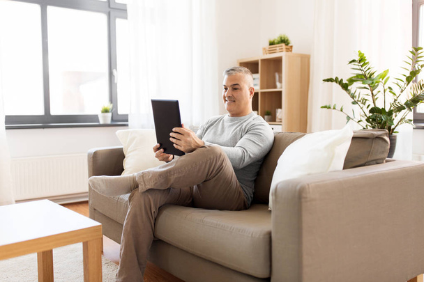 man with tablet pc sitting on sofa at home - Zdjęcie, obraz