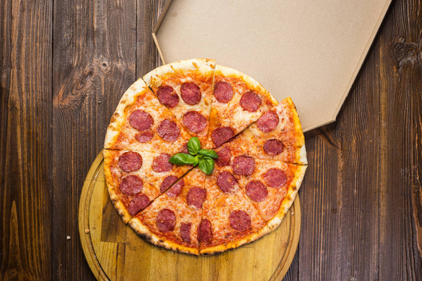 Pizza pepperoni with mozzarella cheese, salami and arugula in box on wooden background - Photo, Image