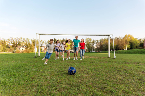Семья играет в футбол на поле. Взрослые и дети гоняются за футбольным мячом по полю. Открытый футбол
 - Фото, изображение