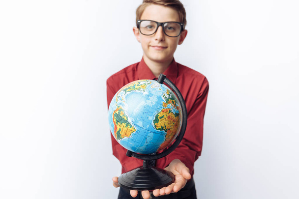 Portrait of positive and emotional schoolboy, with globe, white background, glasses, red shirt, business theme, - Foto, Imagen