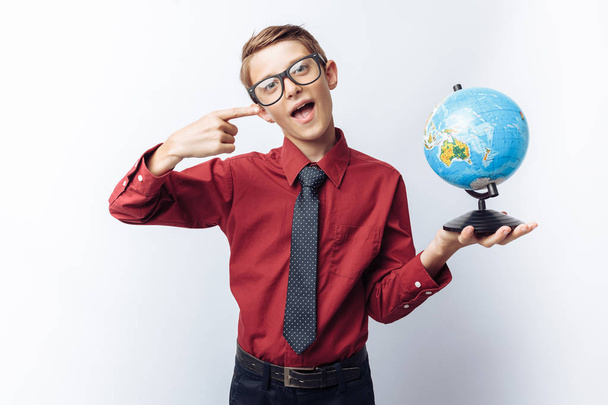 Portrait of positive and emotional schoolboy, with globe, white background, glasses, red shirt, business theme, - Photo, image