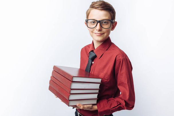Portrait of positive and emotional schoolboy holding books, white background, glasses, red shirt, business theme, - Фото, изображение