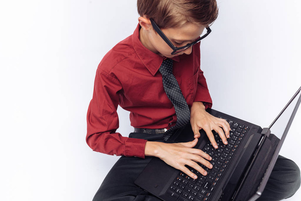 Portrait of positive and emotional schoolboy posing with laptop, typing on keyboard, white background, glasses, red shirt, business theme, - Foto, immagini