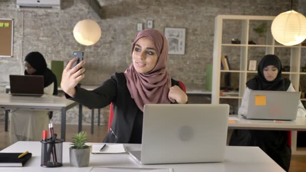 Three young muslim womans in hijab sitting and working in modern office, pretty muslim woman taking selfie with phone, smiling - Metraje, vídeo