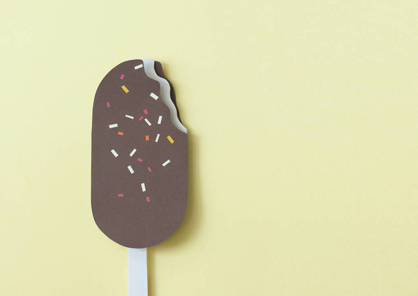 Chocolate ice cream with sprinkles made of paper on yellow pastel background. Minimal paper cut image with copy space. Paper craft. - Foto, immagini