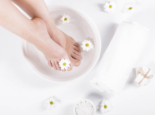 Weibliche Füße mit Wellnessschale, Handtuch und Blumen auf weißem Hintergrund - Foto, Bild