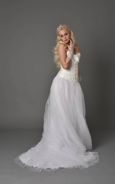 full length portrait of blonde girl wearing white corset gown. standing pose on grey studio background. - Photo, Image