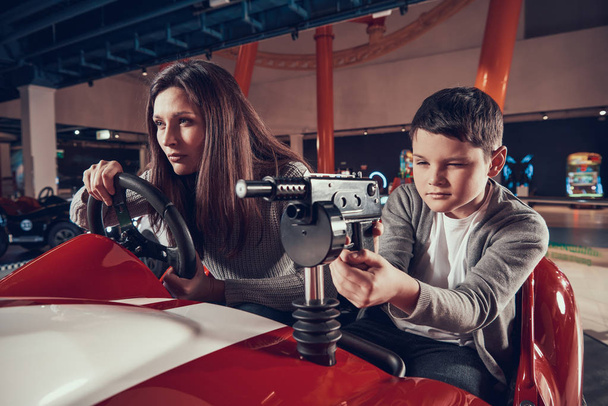 Concentrated mother and son driving toy car. Spending holiday together with family. Entertainment center, mall, amusement park. Family rest, leisure concept. - Fotó, kép