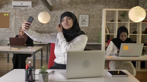 Three young muslim womens in hijab working in modern office, while other muslim woman take selfie with smartphone - Кадри, відео