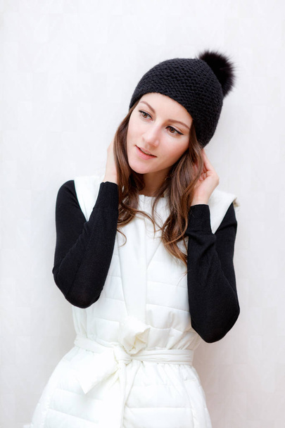 Hipster Style Brunette Girl Swag indossa un cappello nero in maglia con pompon. Posa su uno sfondo bianco armadio in legno. Collezione Autunno Inverno Stagione
 - Foto, immagini