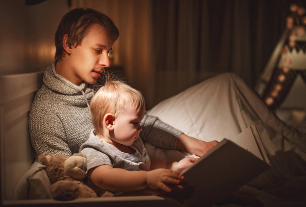 Βραδινό οικογενειακό διάβασμα. Ο πατέρας διαβάζει στα παιδιά ένα βιβλίο πριν πάει για ύπνο. - Φωτογραφία, εικόνα