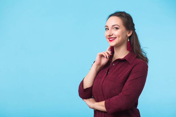 Vrolijke jonge mooie brunette Kaukasische student meisje met lang haar in casual outfit glimlachend fel op blauwe achtergrond met kopie ruimte - Foto, afbeelding