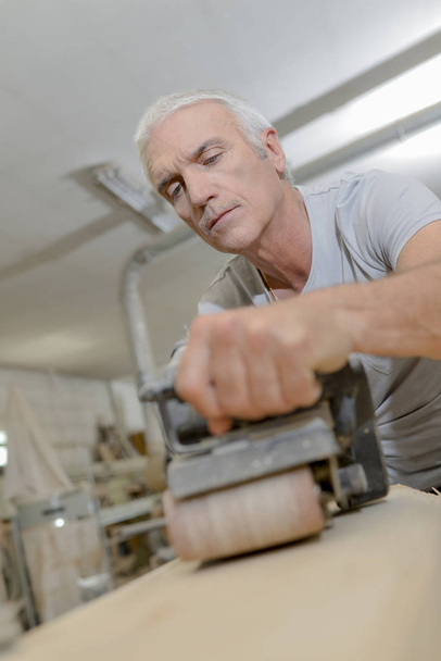 Carpintero mayor usando una lijadora de cinturón
 - Foto, imagen